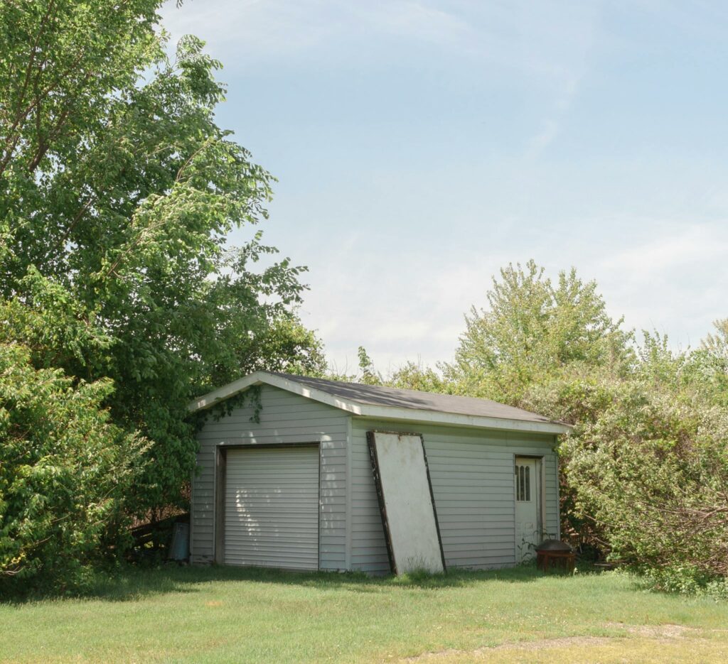 A quaint backyard shed nestled among leafy trees under a clear blue sky, creating a serene outdoor setting.