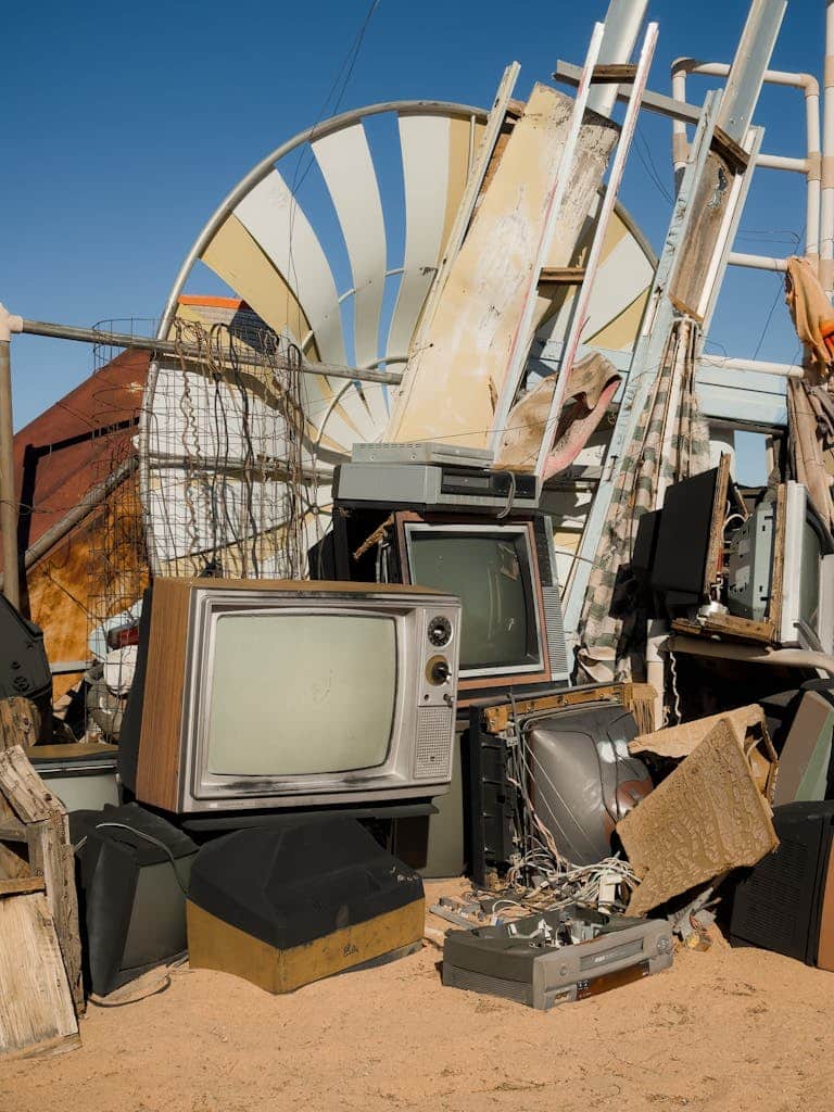 An array of old televisions scattered in the sandy landscape of Joshua Tree junkyard.