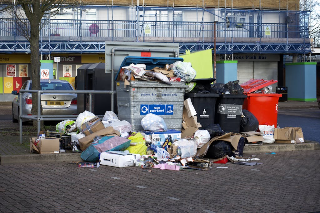 An urban scene depicting overflowing bins and garbage in a parking lot, indicating waste management issues.